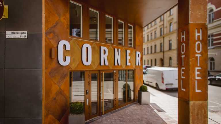 Hotel entrance made of Corten steel, featuring glass panels and a sign in natural light